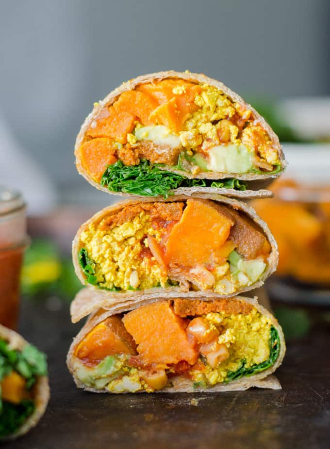 a stack of three vegan breakfast wraps on a dark wooden counter top 