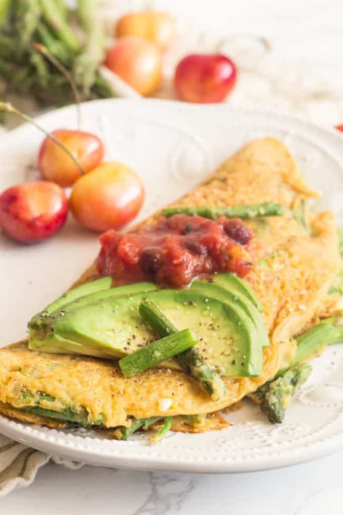 a vegan omelette on a white plate with green asparagus and avocado slices on top 
