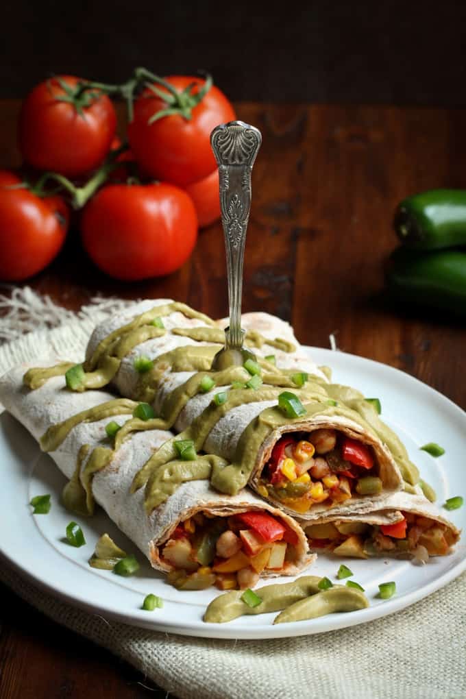 two vegan Mexican breakfast burritos on a white plate with tomatoes in the background 