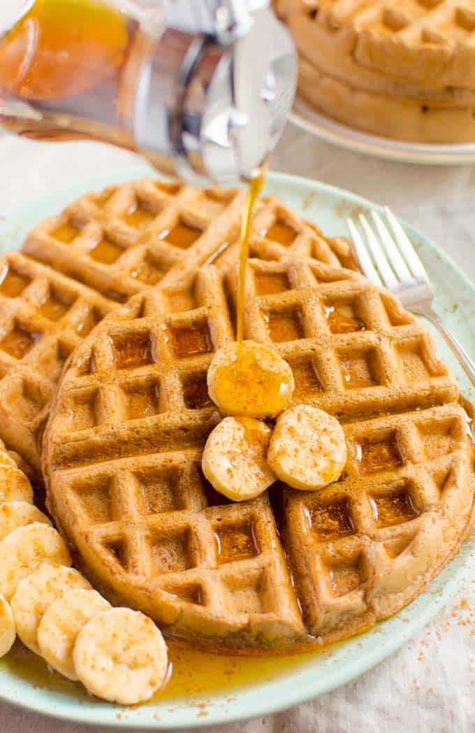 two vegan waffles on a mint green plate with bananas on the side and maple syrup poured on top 