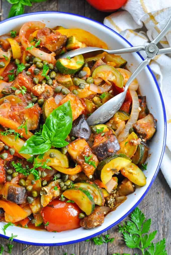 Ratatouille in a blue and white bowl on a wooden counter top with fresh herbs on top and on the side 