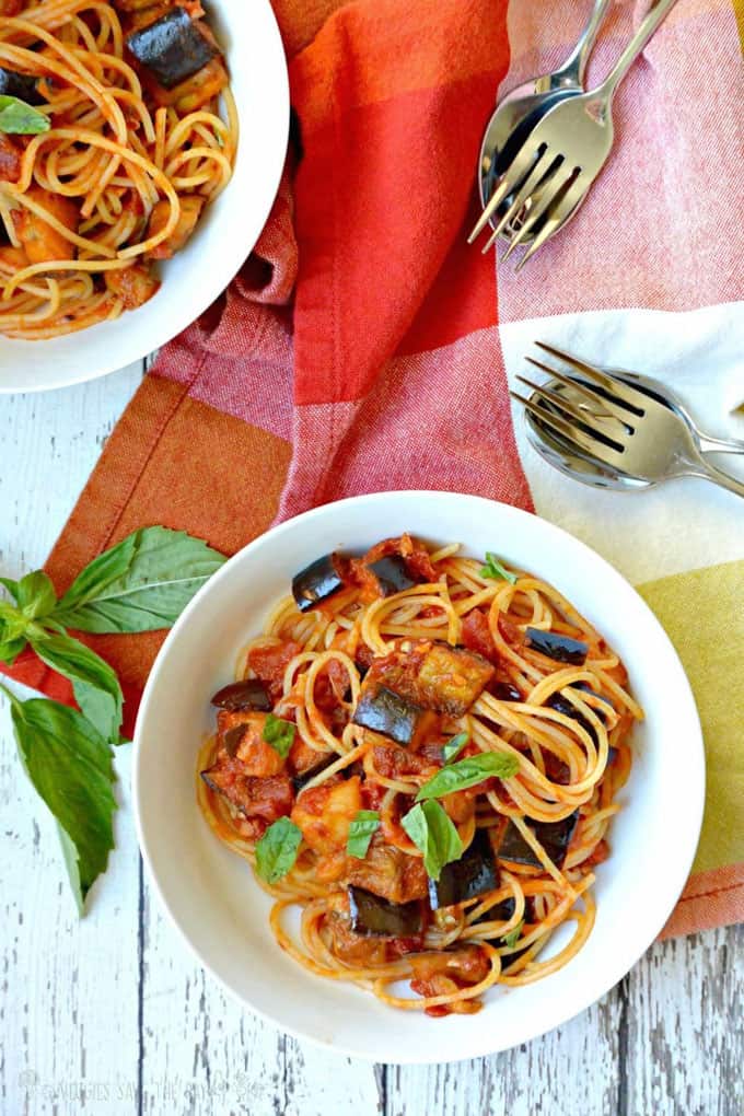 Two Bowls of Eggplant Bolognese Pasta on a white wooden counter top with fresh basil on the side 