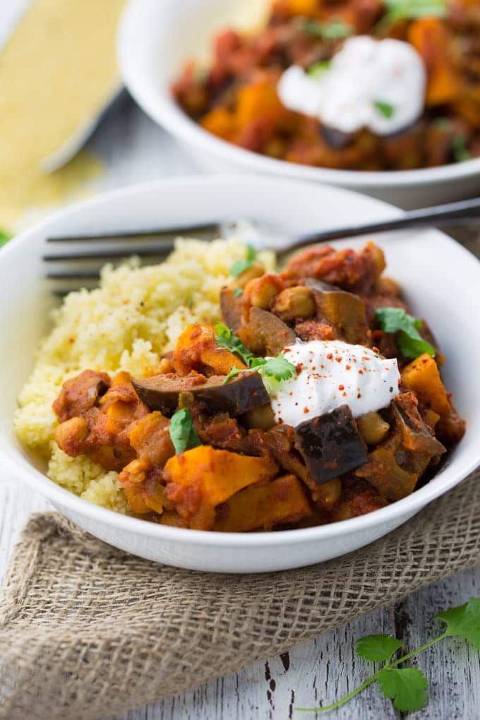 two white bowls of Moroccan chickpea eggplant stew with couscous on a white wooden counter top 