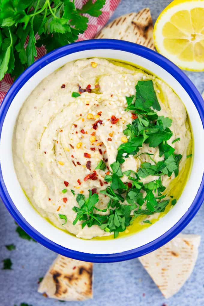 a bowl of Baba Ganoush on a blue counter top with pita slices, parsley, and a lemon half on the side