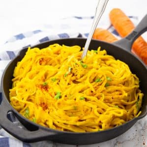 arrot pasta in a cast iron skillet with a fork on a marble counter top with two carrots in the background