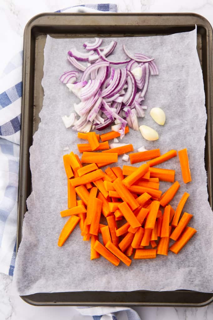 carrot sticks, red onion strips and two cloves of garlic on a baking sheet lined with parchment paper 