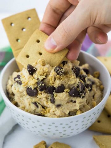 Vegan Cookie Dough in a white bowl with a hand dipping a cookie into the dough