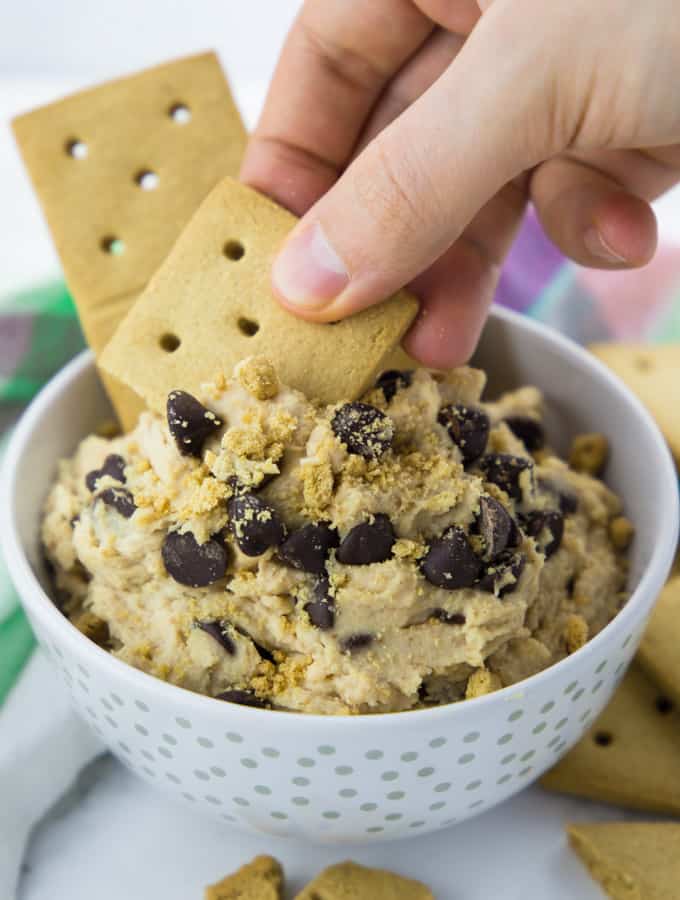 Vegan Cookie Dough in a white bowl with a hand dipping a cookie into the dough