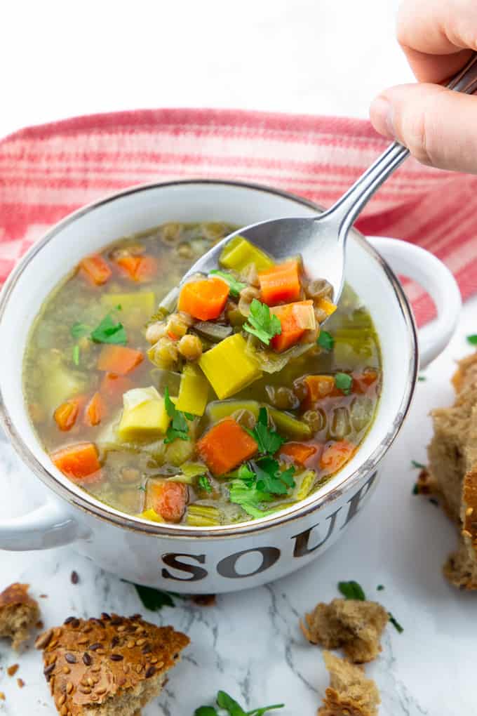 a bowl of vegan lentil soup with a hand holding a spoon with soup over the bowl 