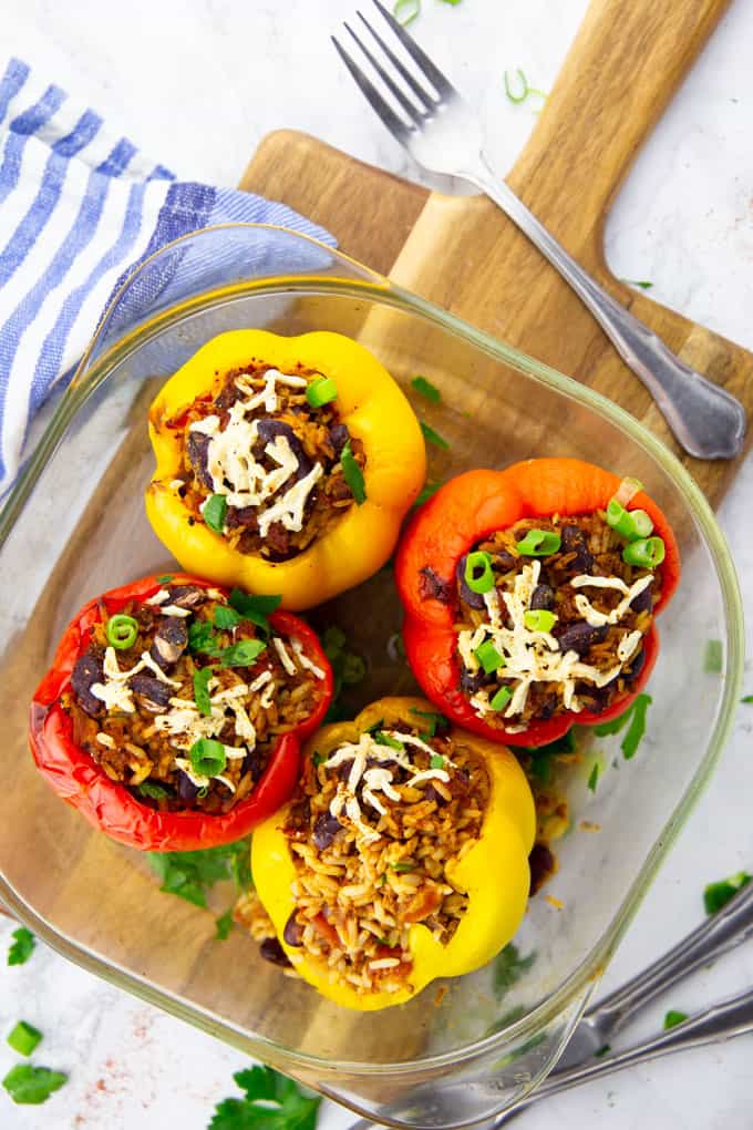 Four Vegan Stuffed Peppers in a glass baking dish on a wooden board with cutlery on the side 