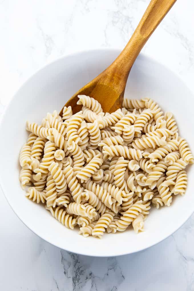 rotini pasta in a white bowl on a marble counter top 