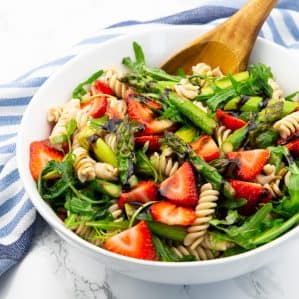 Asparagus Pasta Salad in a white bowl with a wooden spoon on a marble countertop