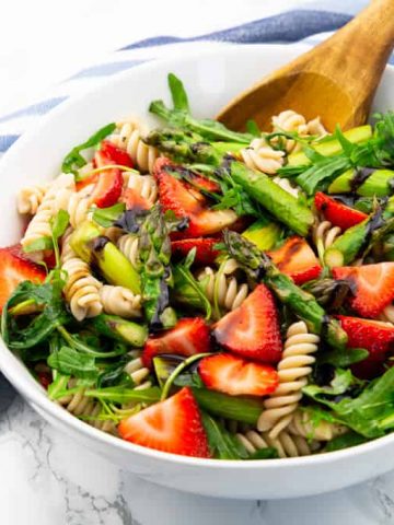 Asparagus Pasta Salad in a white bowl with a wooden spoon on a marble countertop