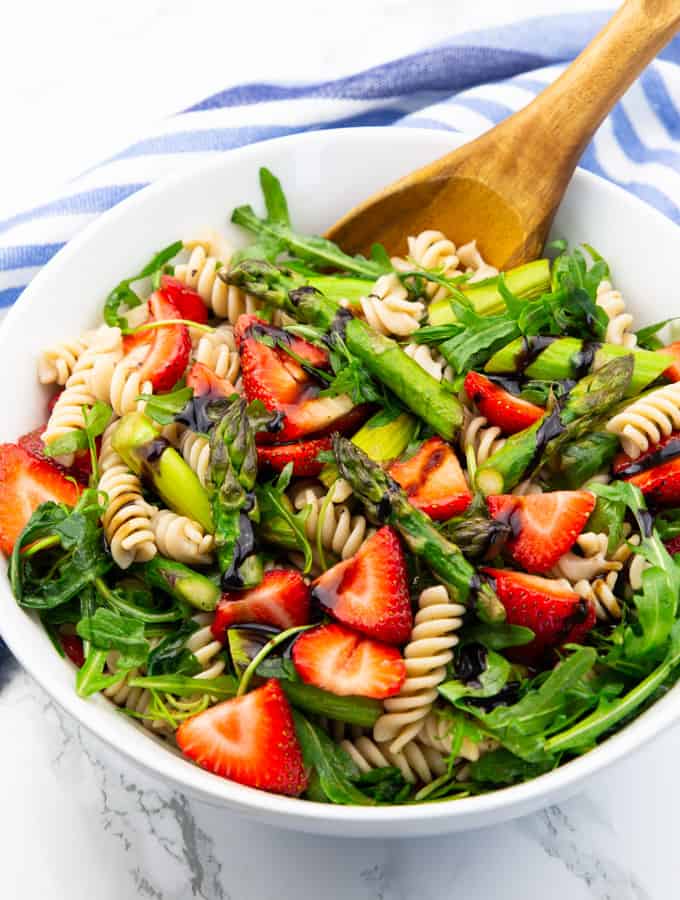 Asparagus Pasta Salad in a white bowl with a wooden spoon on a marble countertop 