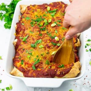 Vegan Enchiladas in a white casserole dish with fresh parsley and limes in the background