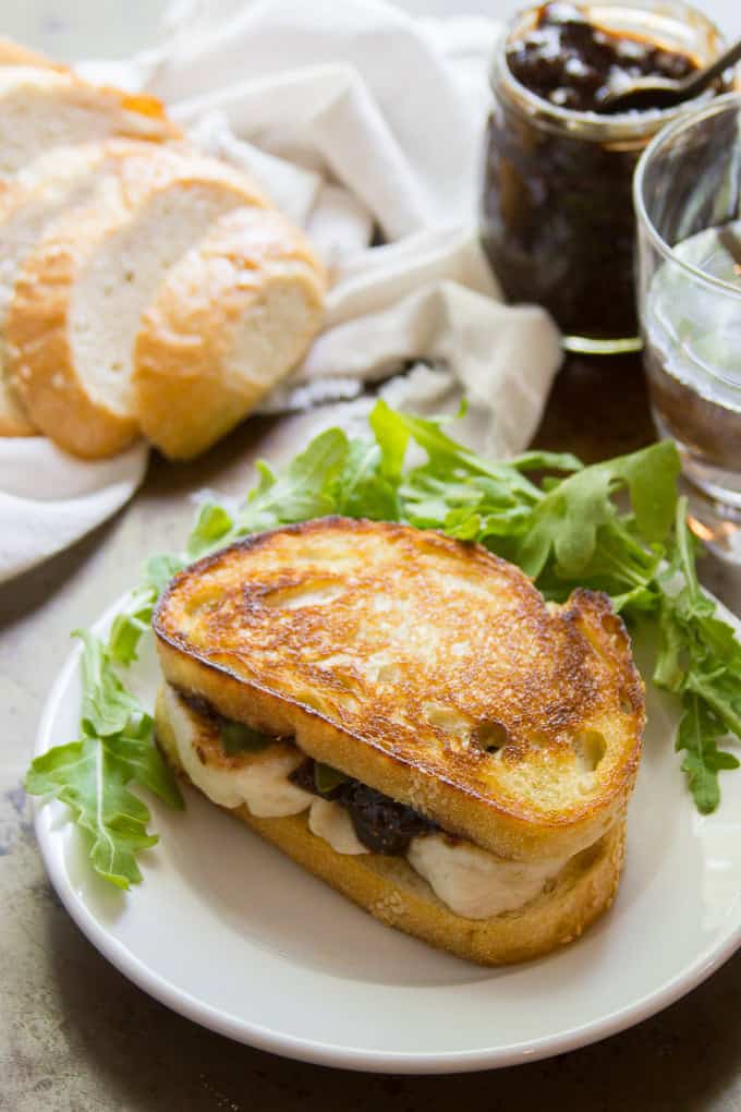 A Vegan Mozzarella & Fig Jam Grilled Cheese Sandwich with a Jar of Fig Jam and Slices of White Bread in the Background