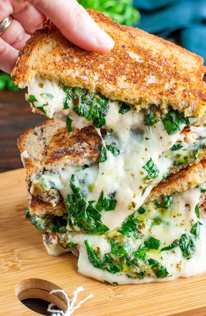 a stack of vegan spinach pesto grilled cheese sandwiches with a hand picking one up 