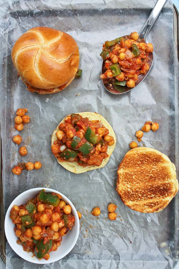 Two Chickpea Sloppy Joes on a baking sheet lined with parchment paper with a spoon and a bowl of the filling on the side 