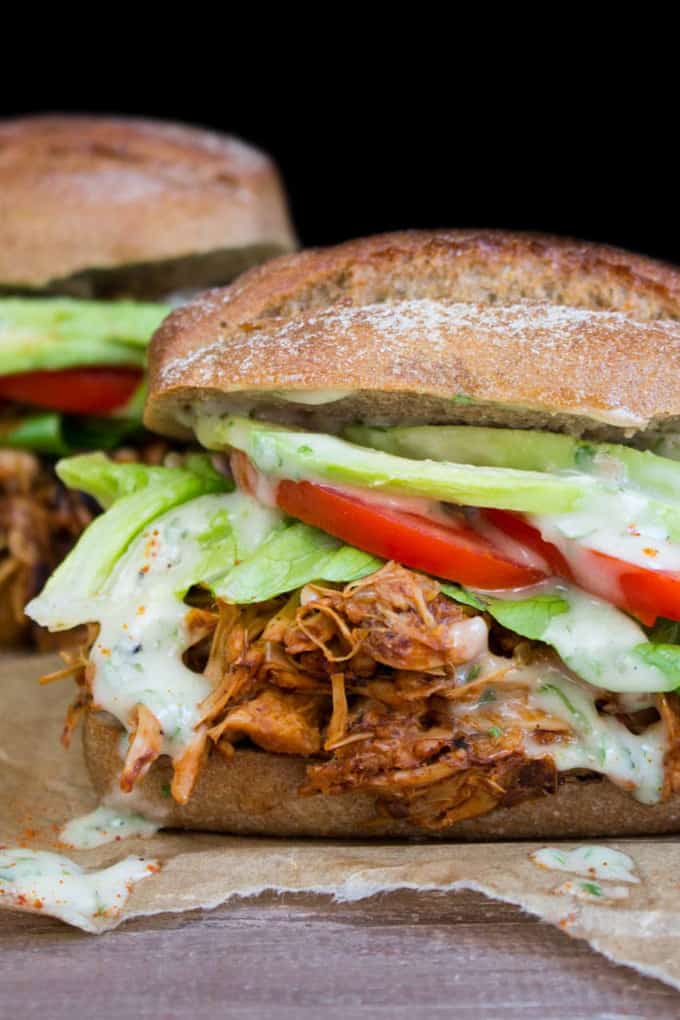 two vegan jackfruit sandwiches with tomato, lettuce, and avocado on a wooden countertop 