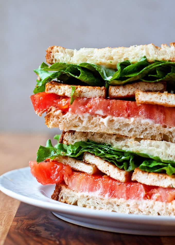 a stack of tofu lettuce tomato sandwiches on a white plate