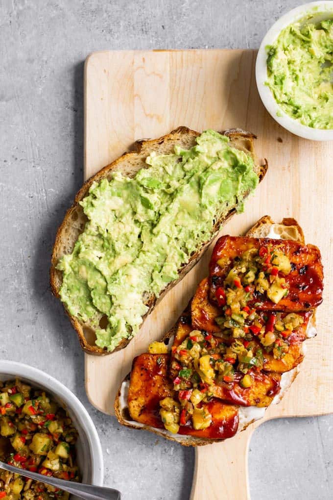 Two Slices of Barbecue Tofu Sandwiches with Pineapple Relish on a wooden board with two bowls of guacamole and pineapple relish on the side