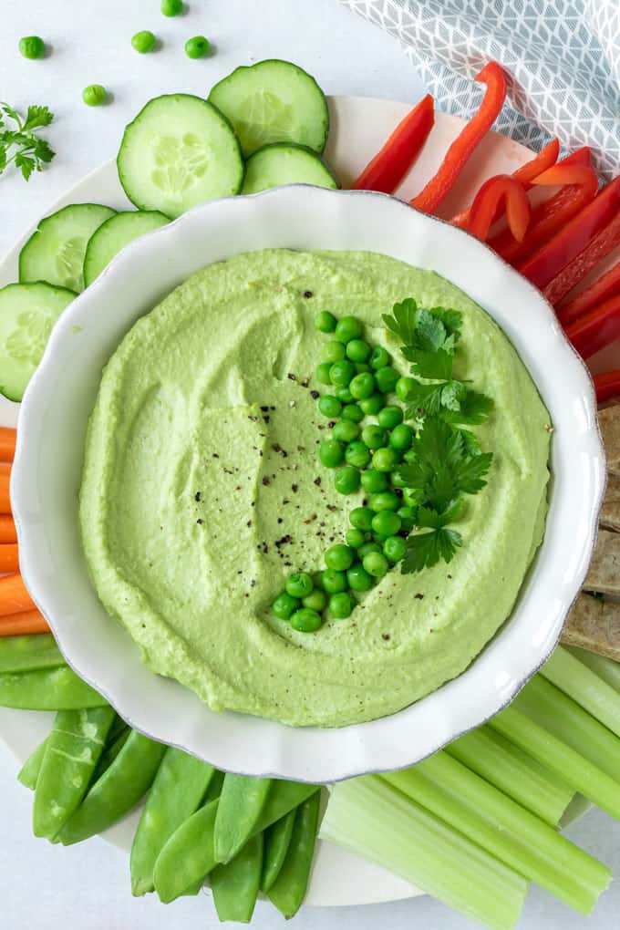 Pea Hummus in a white bowl with veggie sticks on the side 