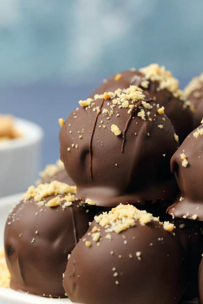 a pile of Chocolate Peanut Butter Balls on a white plate with a blue background 