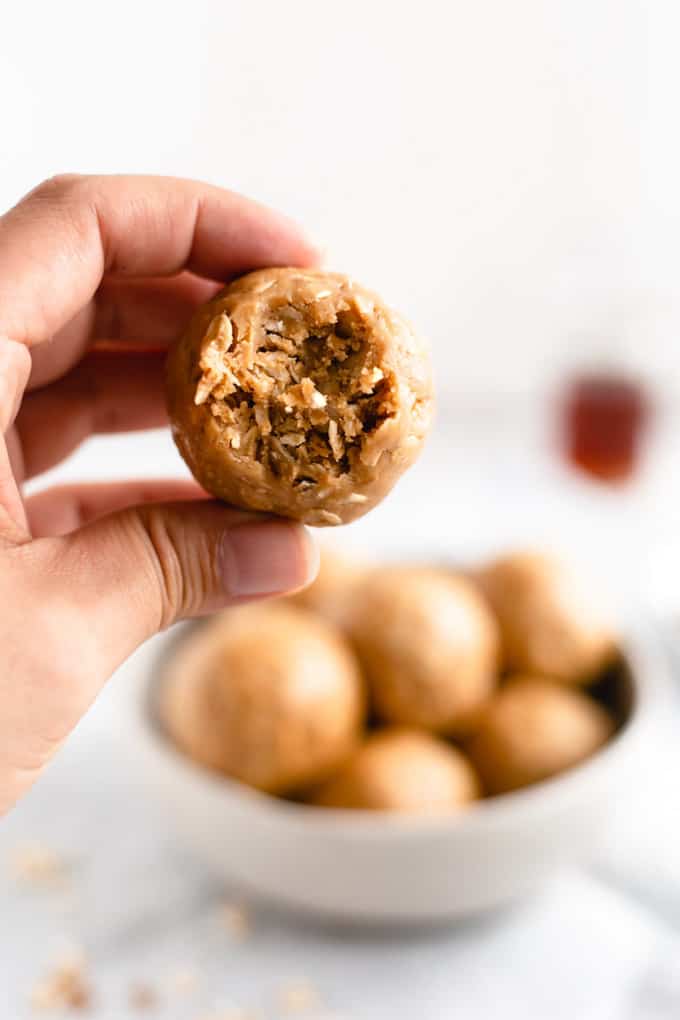 a hand Coconut and Peanut Butter Spiced Energy Bite with a bowl of more energy bites in the background