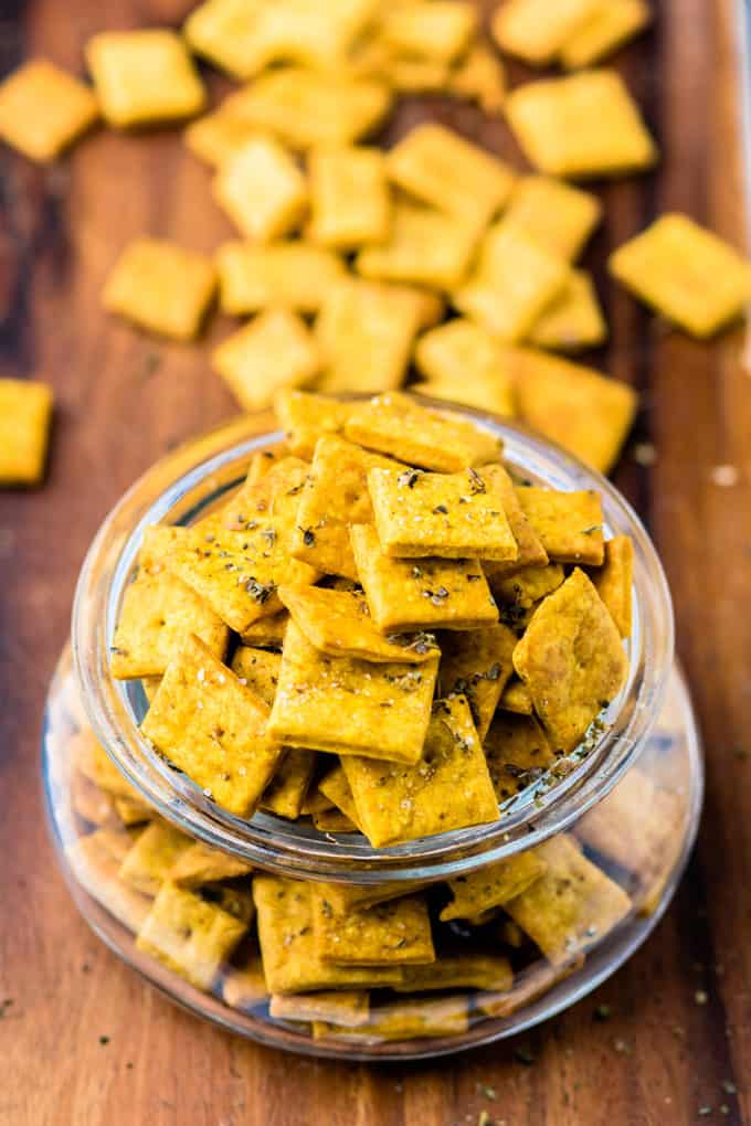 vegan cheese crackers in a glass jar on a wooden board with more crackers in the background