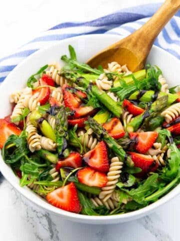 Asparagus Pasta Salad in a white bowl with a wooden spoon on a marble countertop
