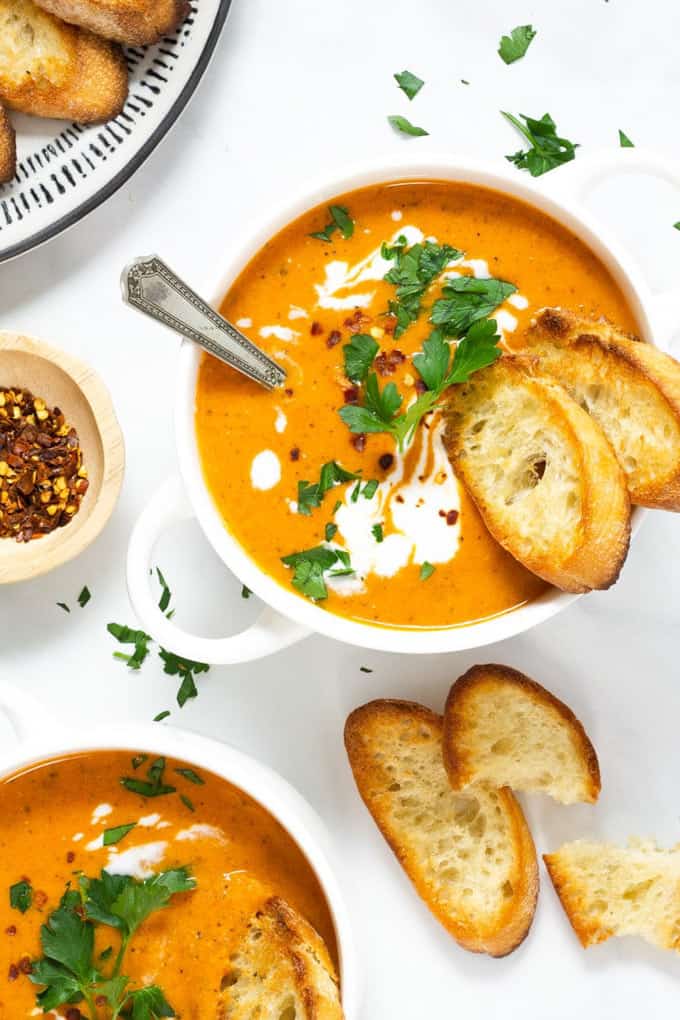 Two bowls with vegan tomato soup with roasted bread on a white countertop 