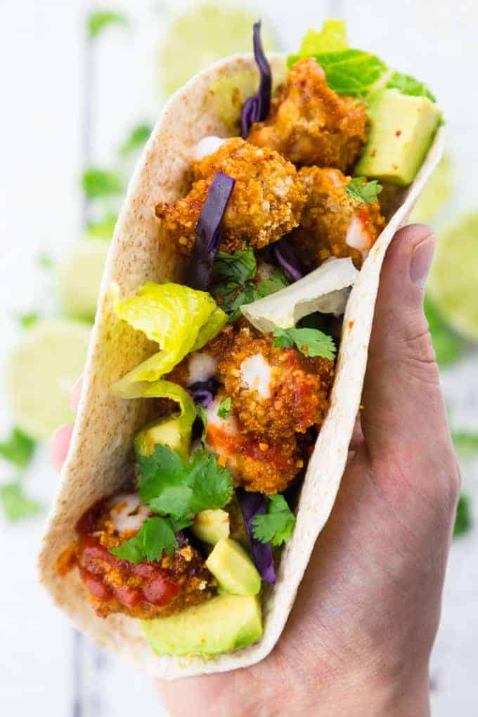 a hand holding a taco filled with cauliflower wings, avocado, and lettuce 