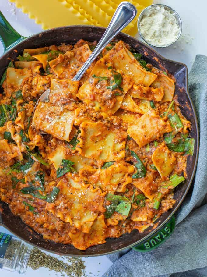 Vegan “Beefy” Skillet Lasagna in a black pan with a fork and lasagna sheets and a small bowl of vegan ricotta in the background 