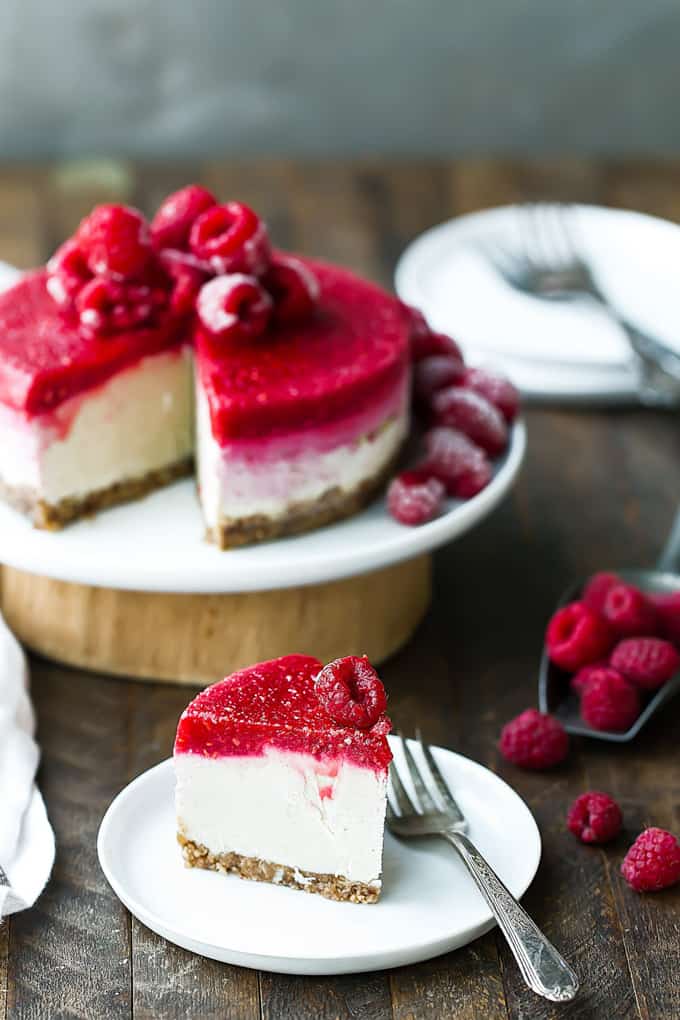 An Easy Vegan Raspberry Cheesecake on white plates on a wooden countertop with raspberries on the side 