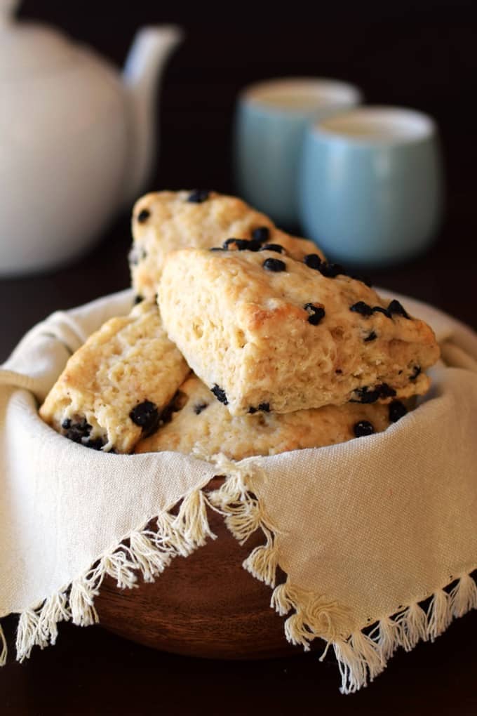 Vegan Wild Blueberry Scones in a basket with two mugs and a can of tea in the background 
