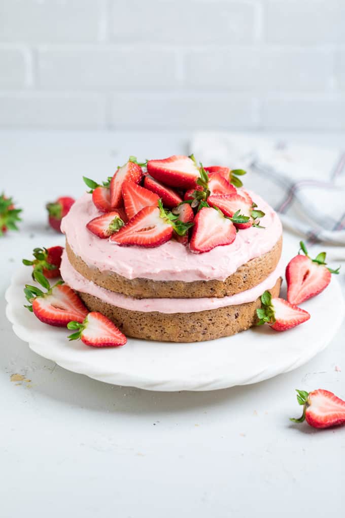 Vegan Strawberry Cake on a white plate with strawberries on the side on a white countertop 
