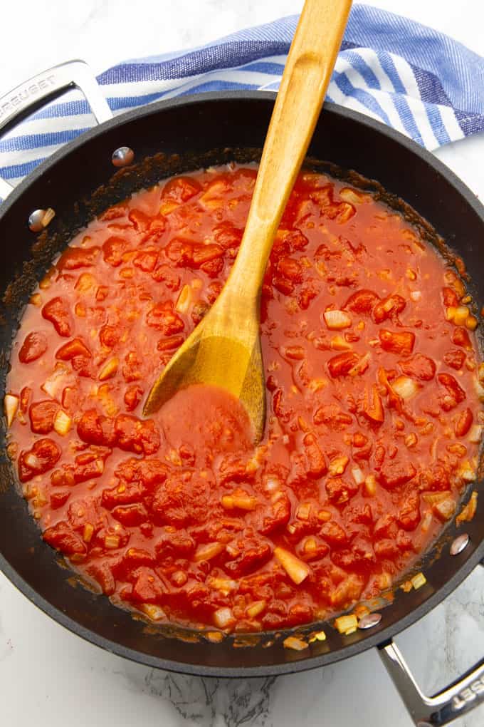 vegan spaghetti sauce in a black pan with a wooden spoon on a marble countertop 