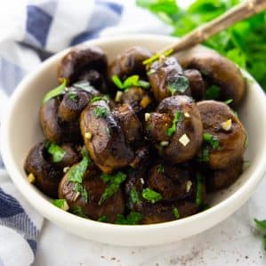 Balsamic Mushrooms in a white bowl with a spoon on a marble countertop with fresh parsley and a blue and white dishcloth in the background