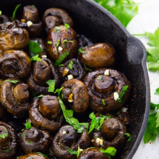 balsamic mushrooms in a cast iron pan sprinkled with chopped parsley on a marble countertop