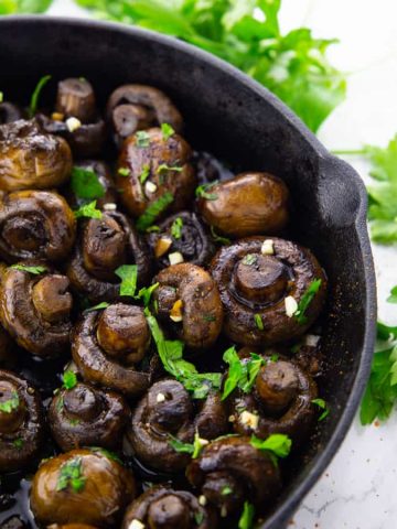 balsamic mushrooms in a cast iron pan sprinkled with chopped parsley on a marble countertop
