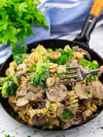broccoli pasta in a black pan with a hand that picks up some of the pasta with a fork