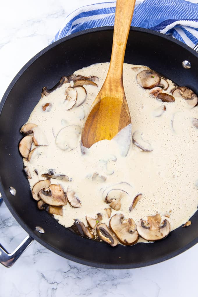 sautéed mushrooms in a black pan with creamy cashew sauce and a wooden spoon on a marble countertop 