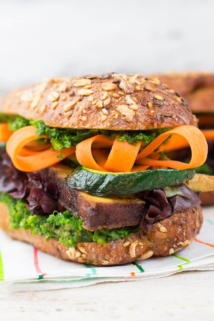 a sandwich with smoked tofu slices, zucchini, carrot, and kale pesto on a white wooden countertop 