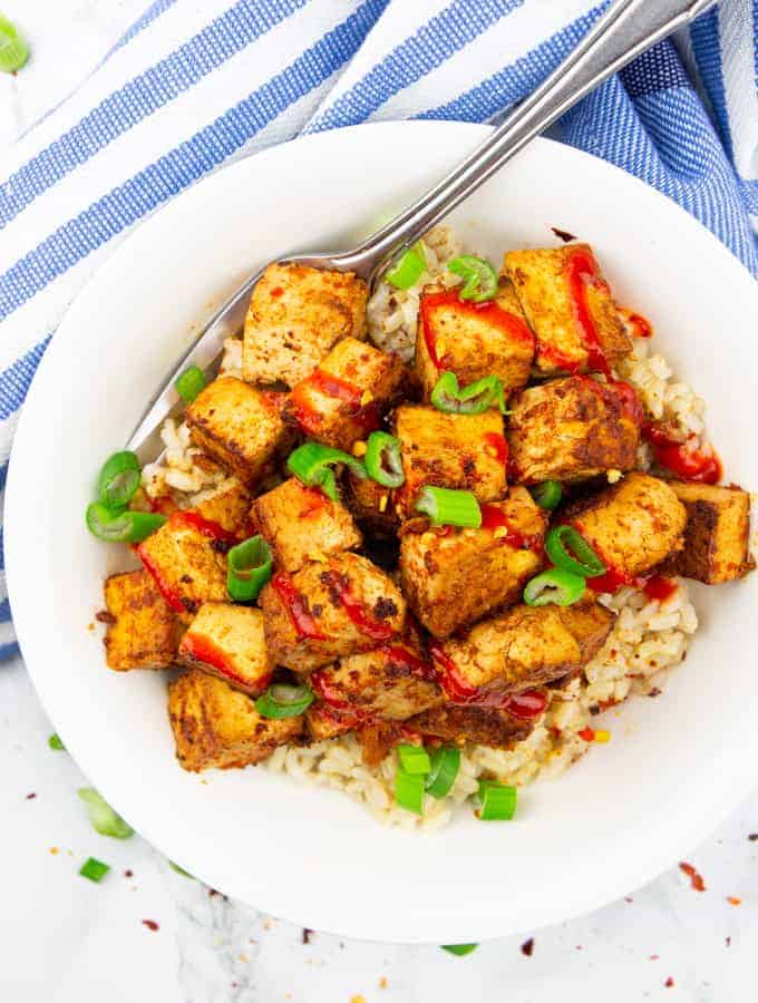 marinated tofu over rice in a white bowl with a fork on a marble countertop 