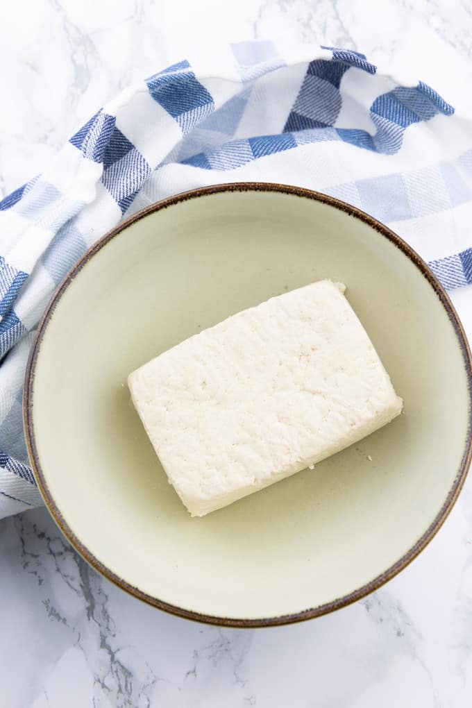 a large piece of tofu in a beige bowl on a marble countertop 