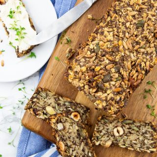a loaf of vegan bread on a wooden cutting board with three slices in front and a slice with cream cheese on a small plate on the side