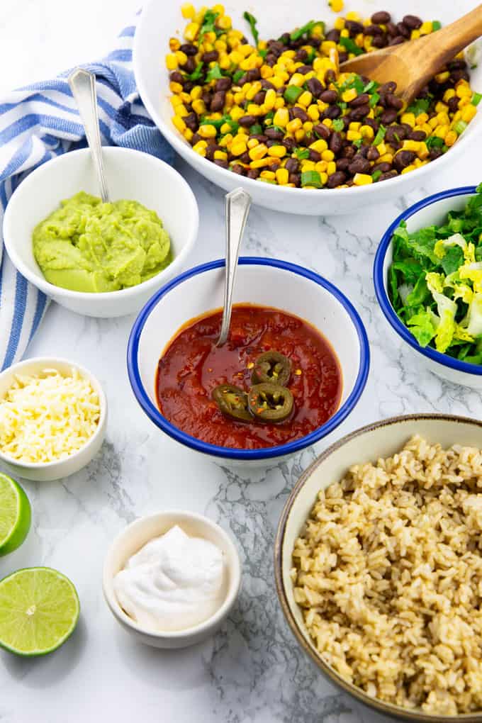 ingredients for burritos in small bowls on a marble countertop 