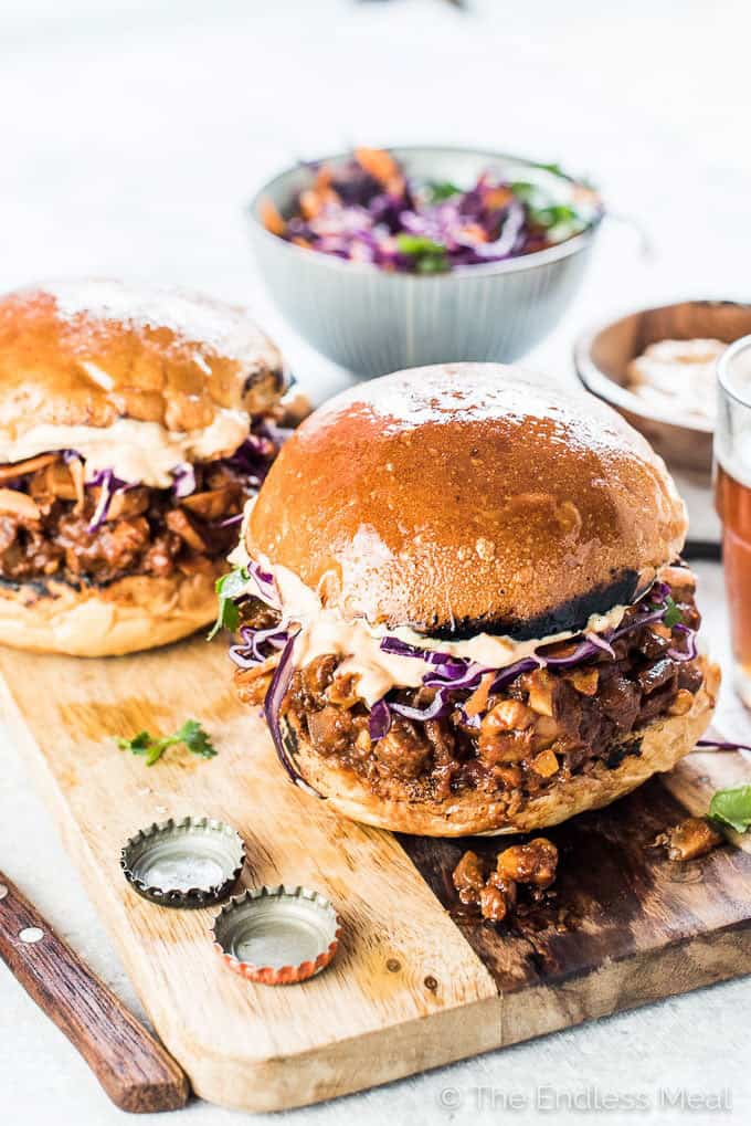 Two Chipotle Mushroom Sloppy Joes on a wooden board with a bowl of slaw in the background 
