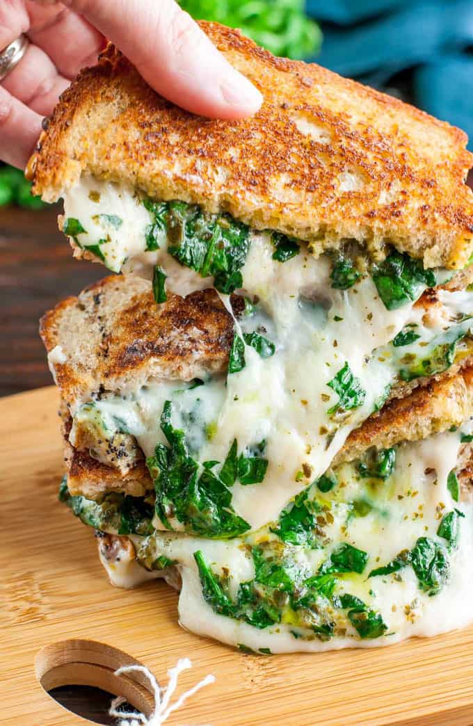 a stack of vegan grilled cheese sandwiches with a hand lifting one of the sandwiches 