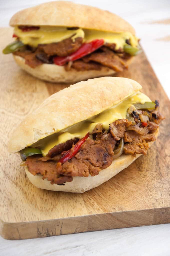 two vegan Philly Cheesesteak sandwiches on a wooden cutting board 
